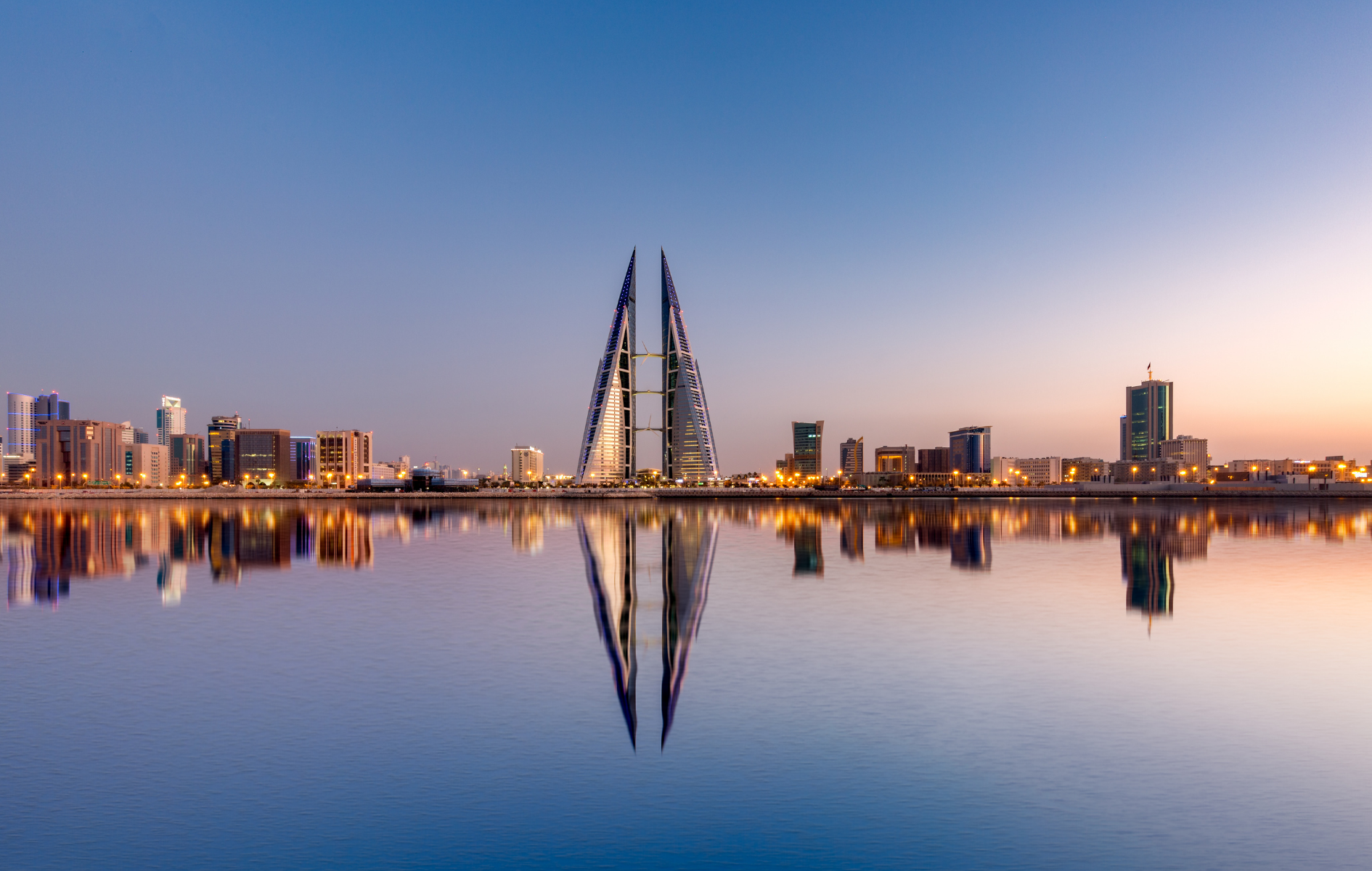 Bahrain skyline with twin skyscrapers reflected in calm water at dawn.