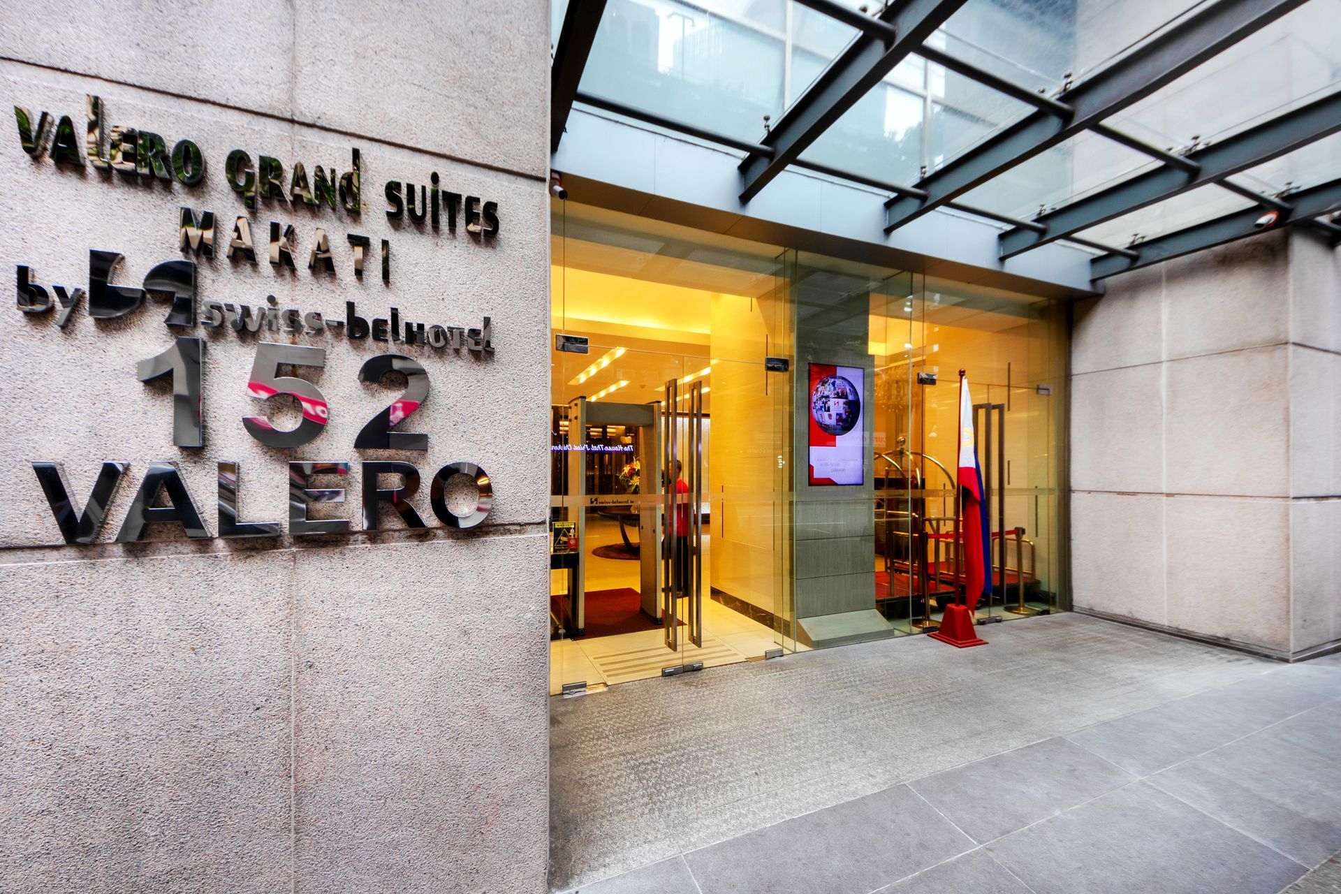 Valero Grand Suites entrance, Makati. Signage on a stone wall, glass doors, and a bright interior.