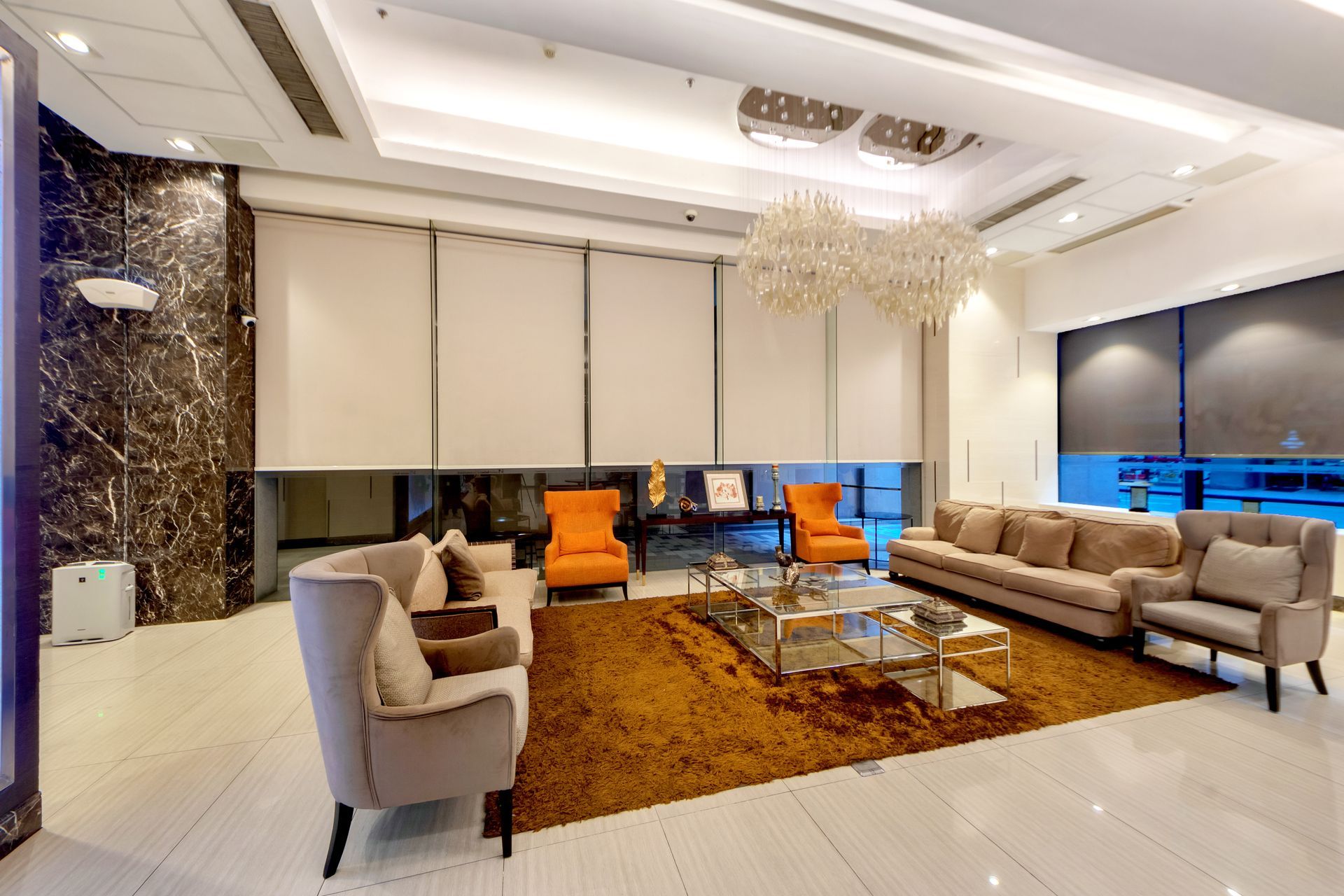 Luxurious waiting area with beige couches, orange chairs, and a gold rug.