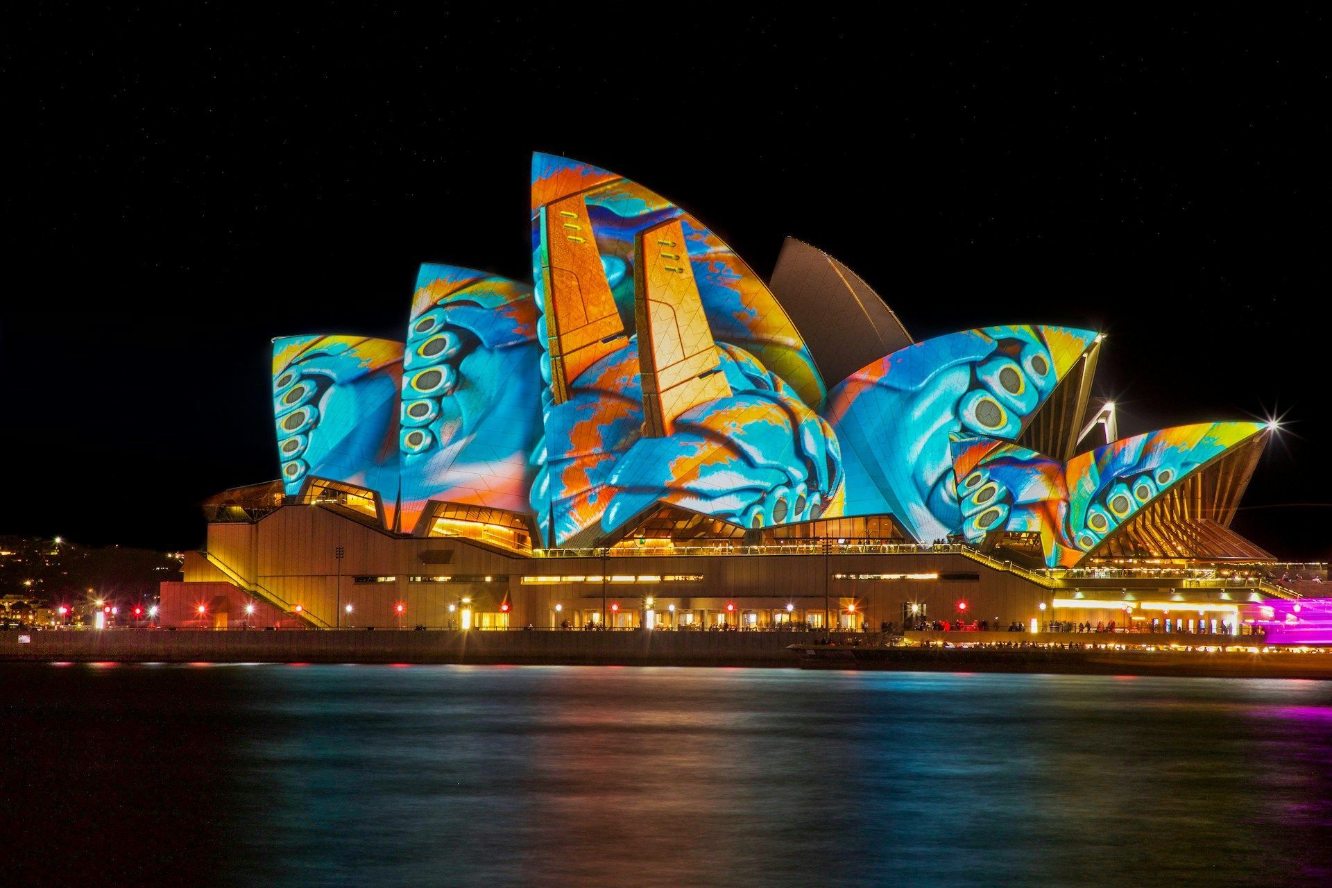Sydney Opera House at night, illuminated with vibrant blue, orange, and yellow artwork.