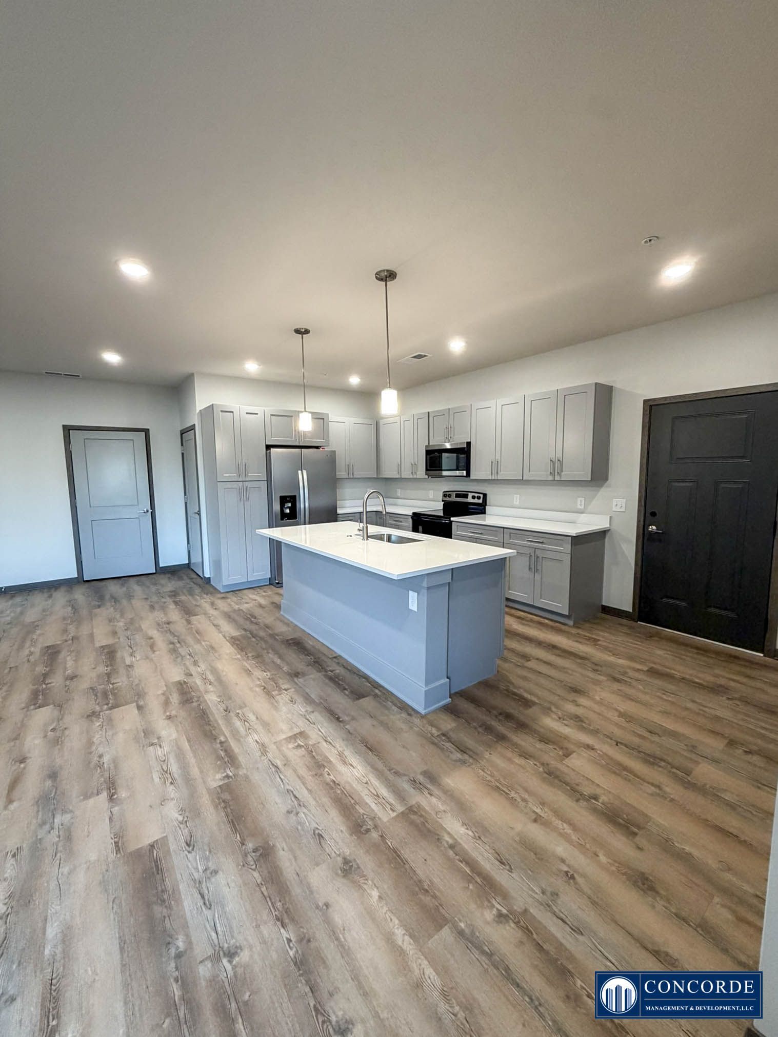 Bright modern kitchen with white cabinets, gray island, stainless appliances, and wood-look flooring.