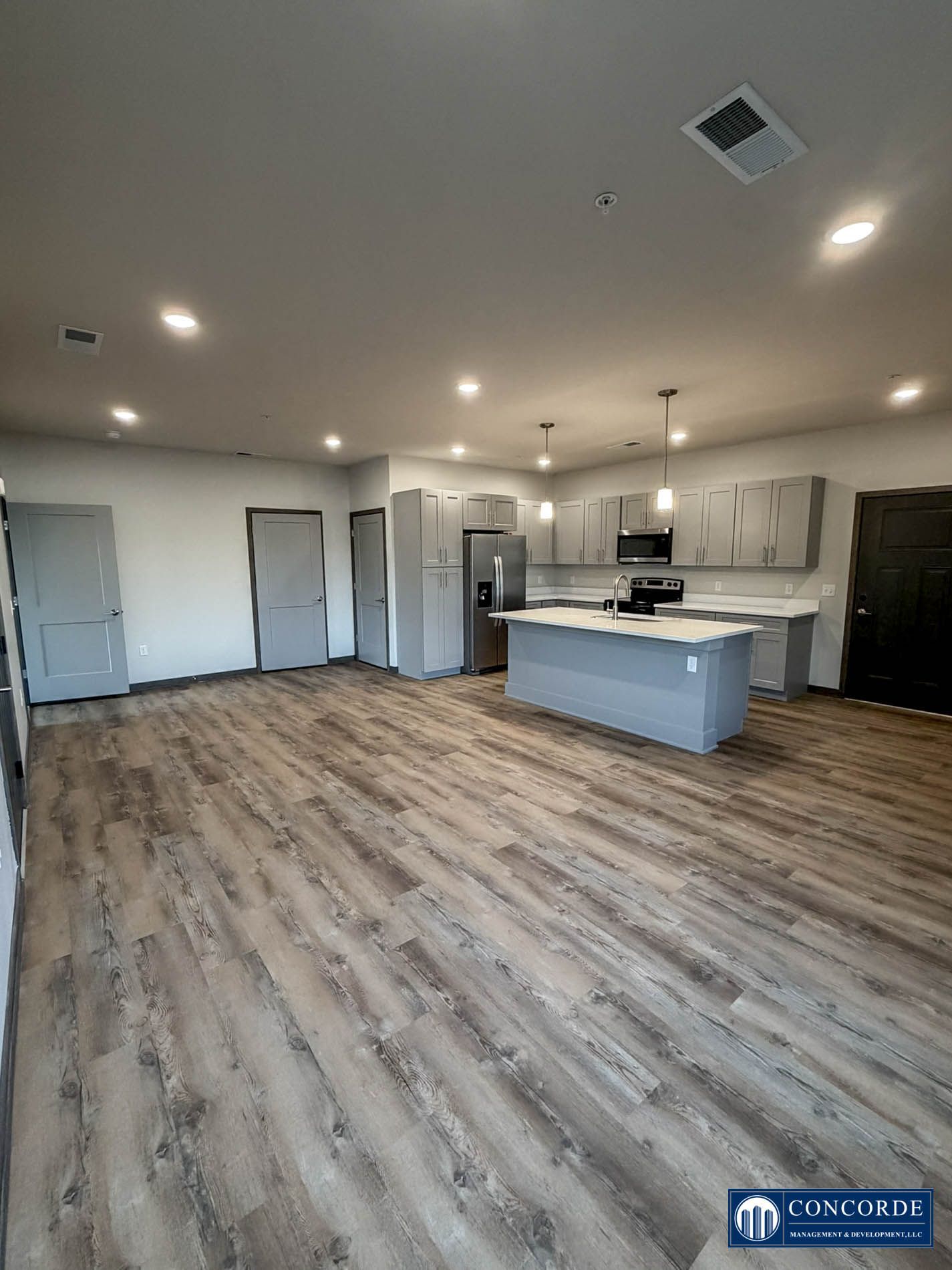 Spacious modern kitchen and living area with wood-look floors, island, recessed lights, and stainless appliances
