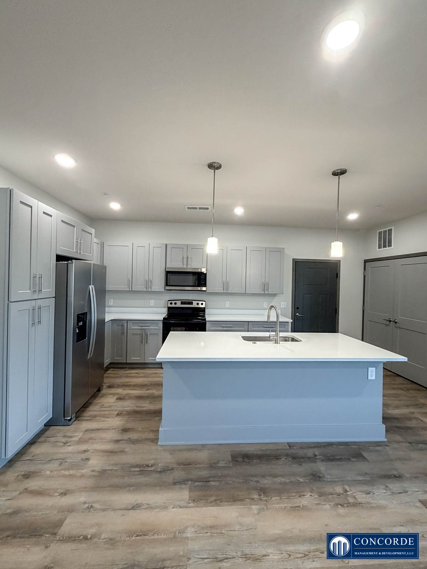 Modern white kitchen with large island, stainless steel appliances, and light wood floors.