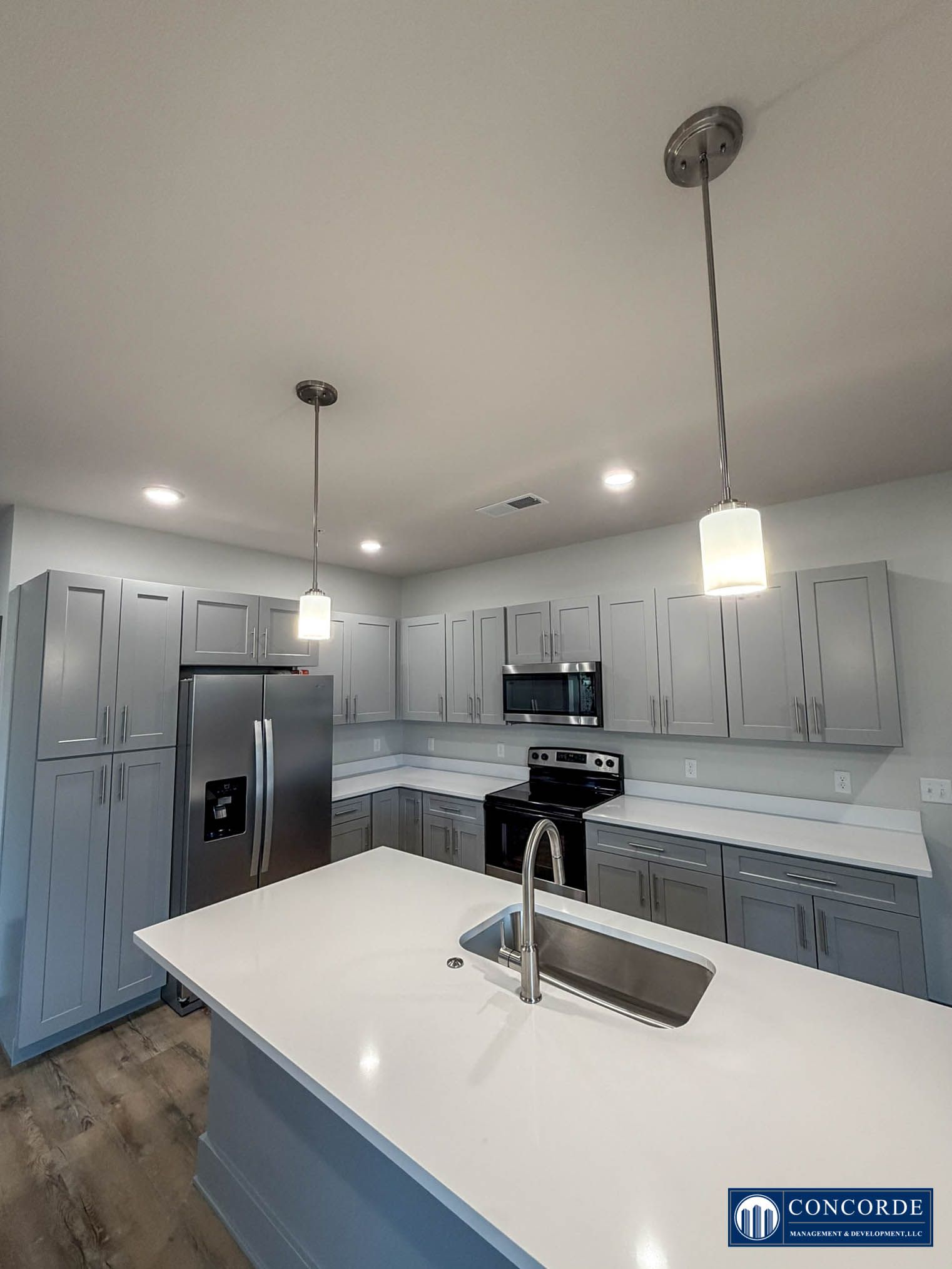Modern gray kitchen with island, pendant light, stainless appliances, and white countertops.