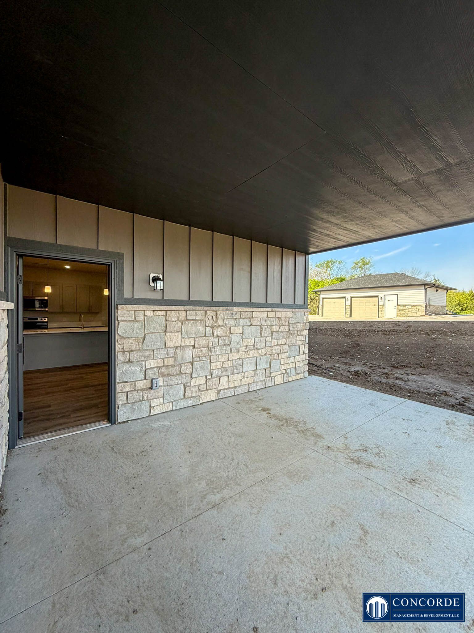Covered patio with stone wall, sliding door, and view of backyard and neighboring homes
