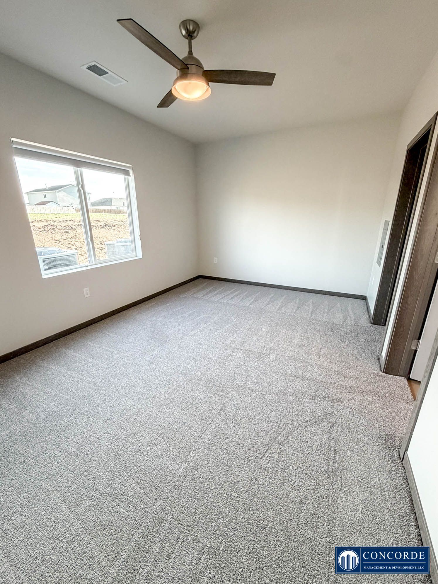 Empty carpeted bedroom with ceiling fan and window, viewed from the doorway