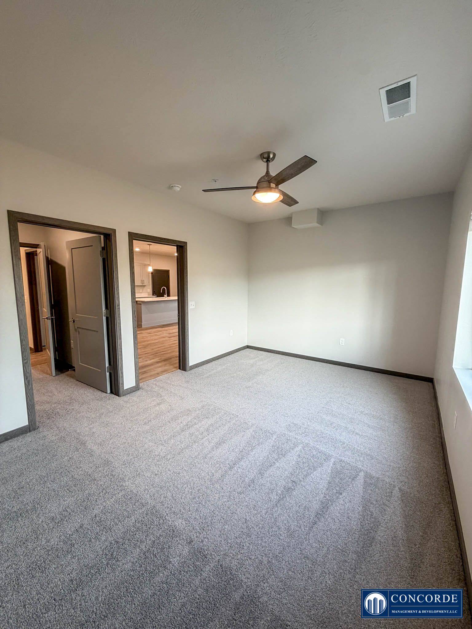 Empty carpeted bedroom with ceiling fan, open closet, and adjoining bathroom doorway