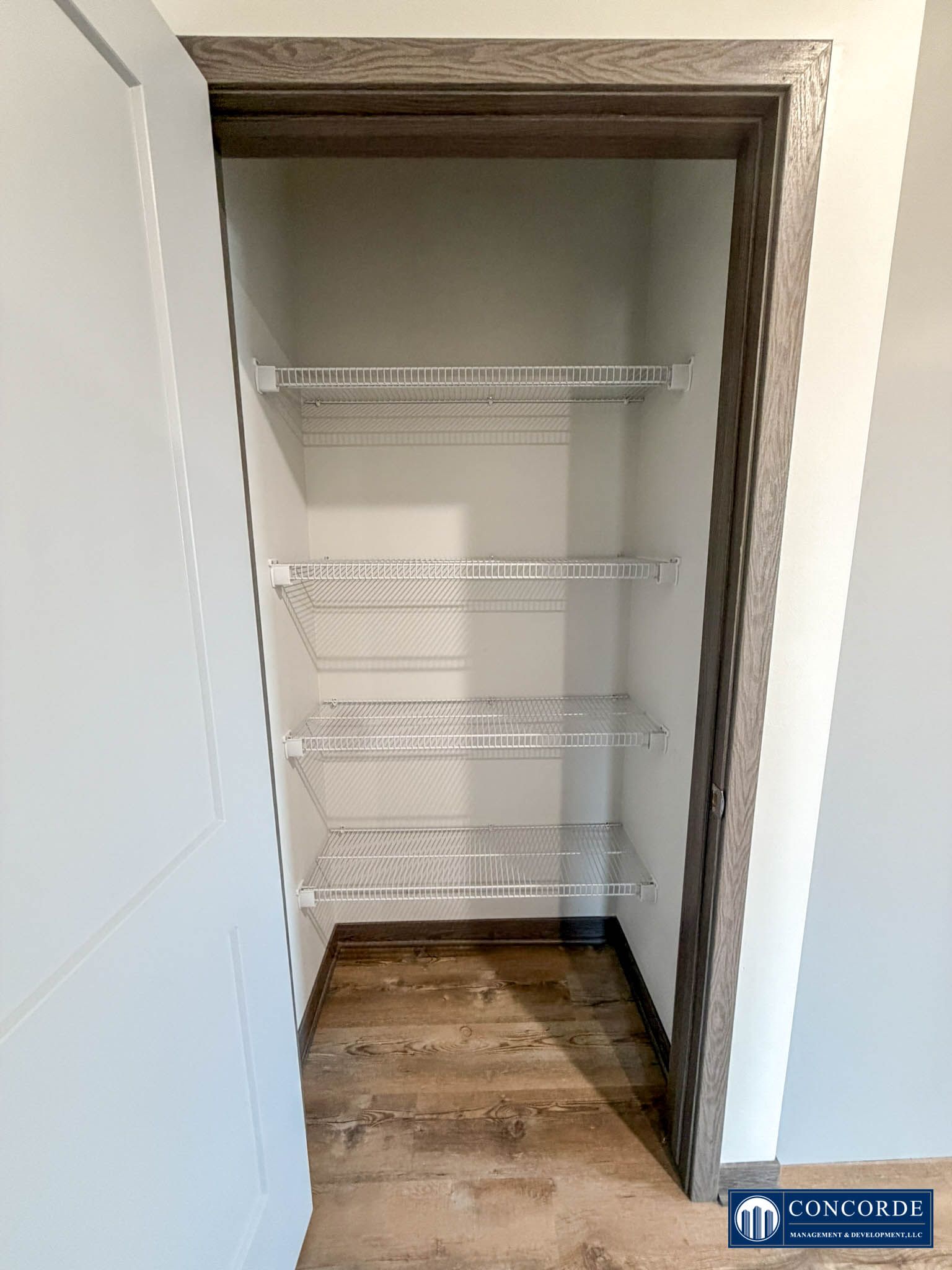 Empty closet with white wire shelves and wood flooring, viewed through an open door.