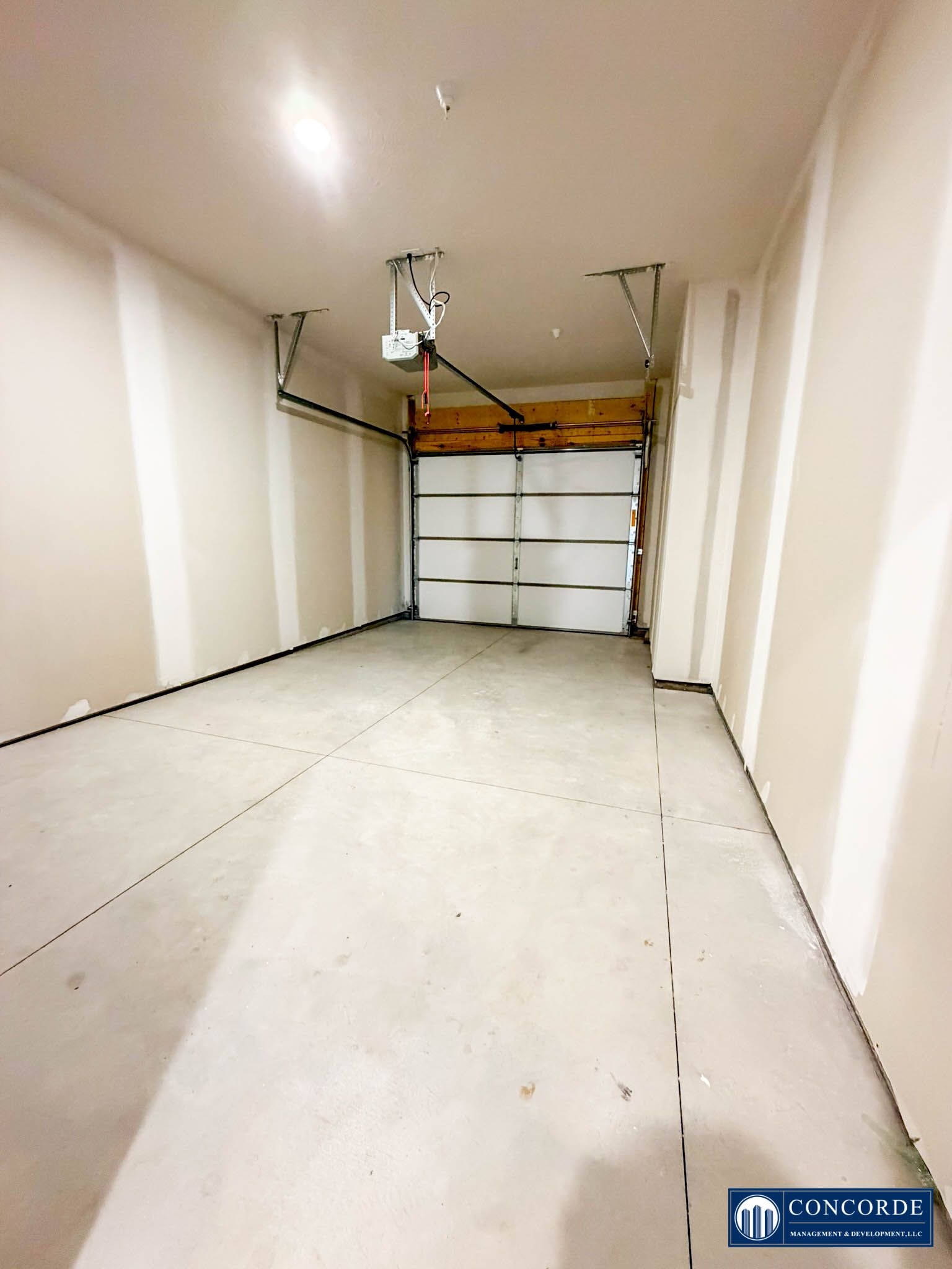 Empty white garage interior with closed garage door and ceiling-mounted opener.
