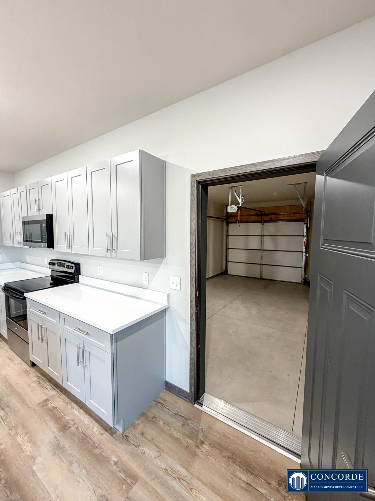 Laundry room with white cabinets, gray counters, and an open doorway to storage shelves.