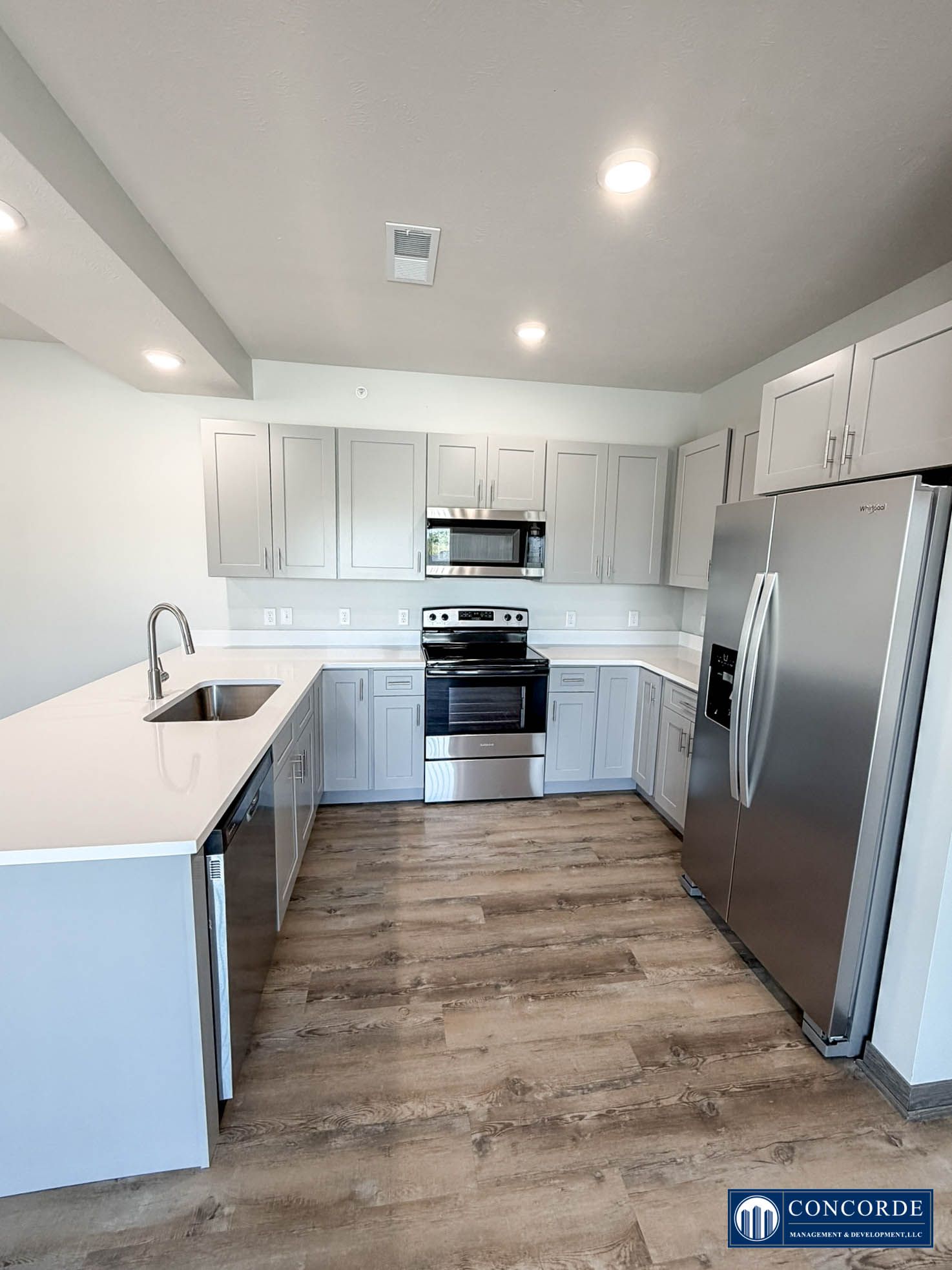 Bright modern kitchen with white cabinets, stainless steel appliances, and wood-look flooring.