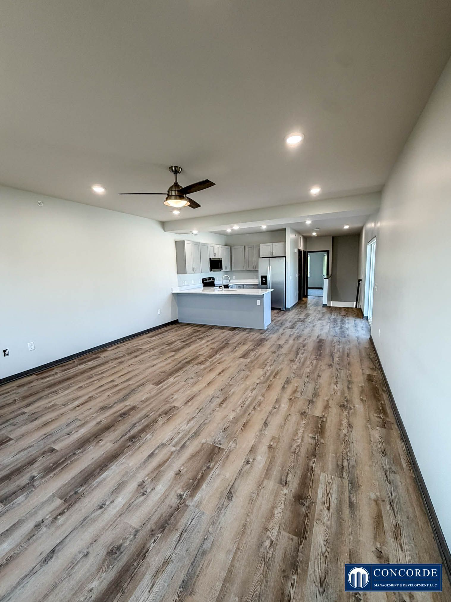 Empty open-plan living room with wood floors, white walls, kitchen island, and ceiling fan