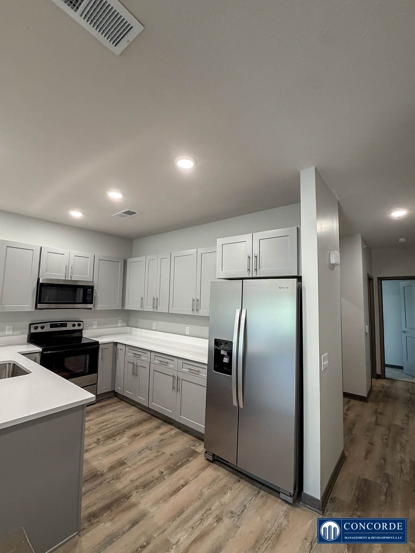 Bright white kitchen with stainless steel appliances, wood floors, and white cabinets.