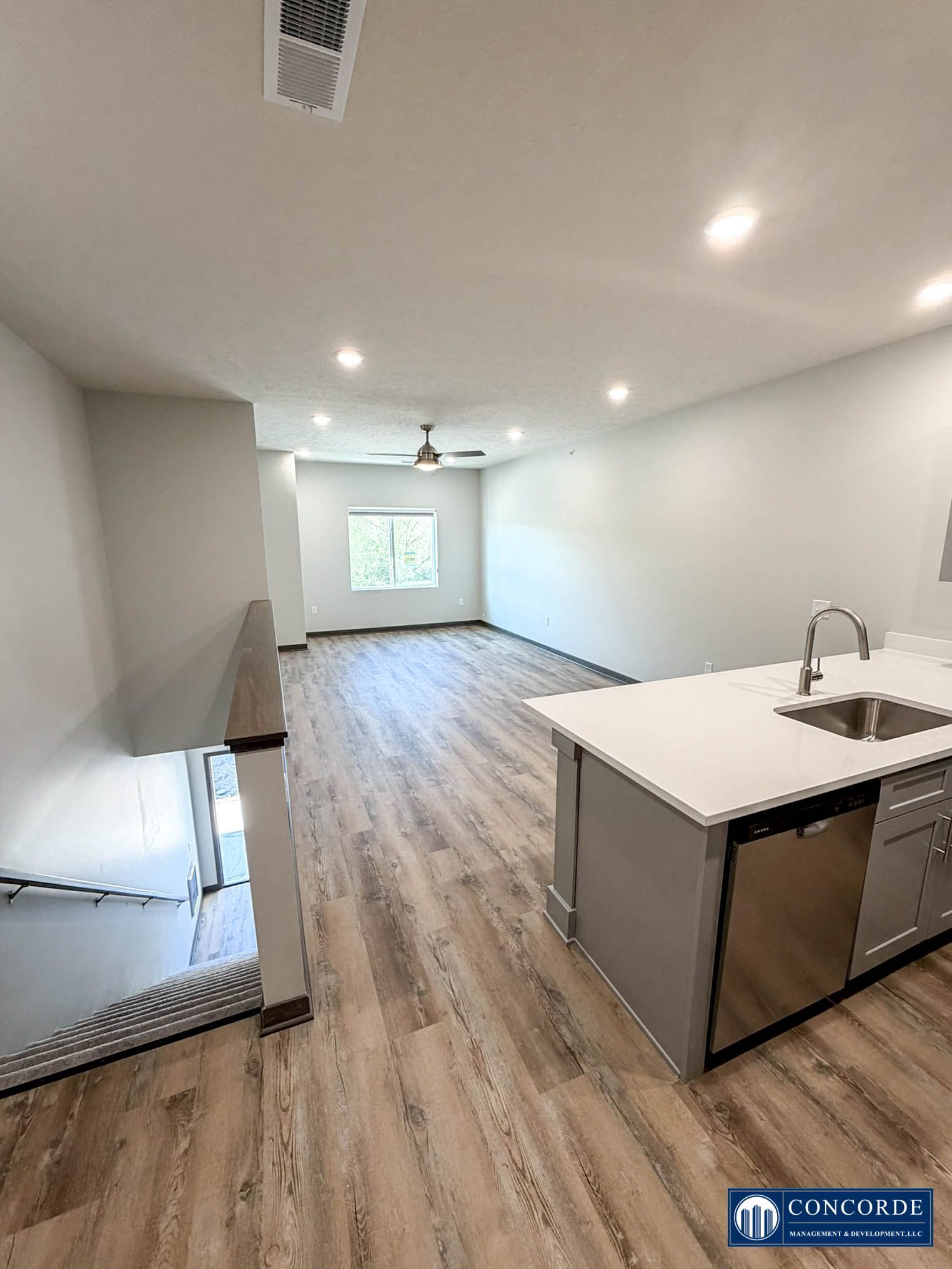 Bright open kitchen-living area with white walls, wood floors, island sink, and ceiling fan.