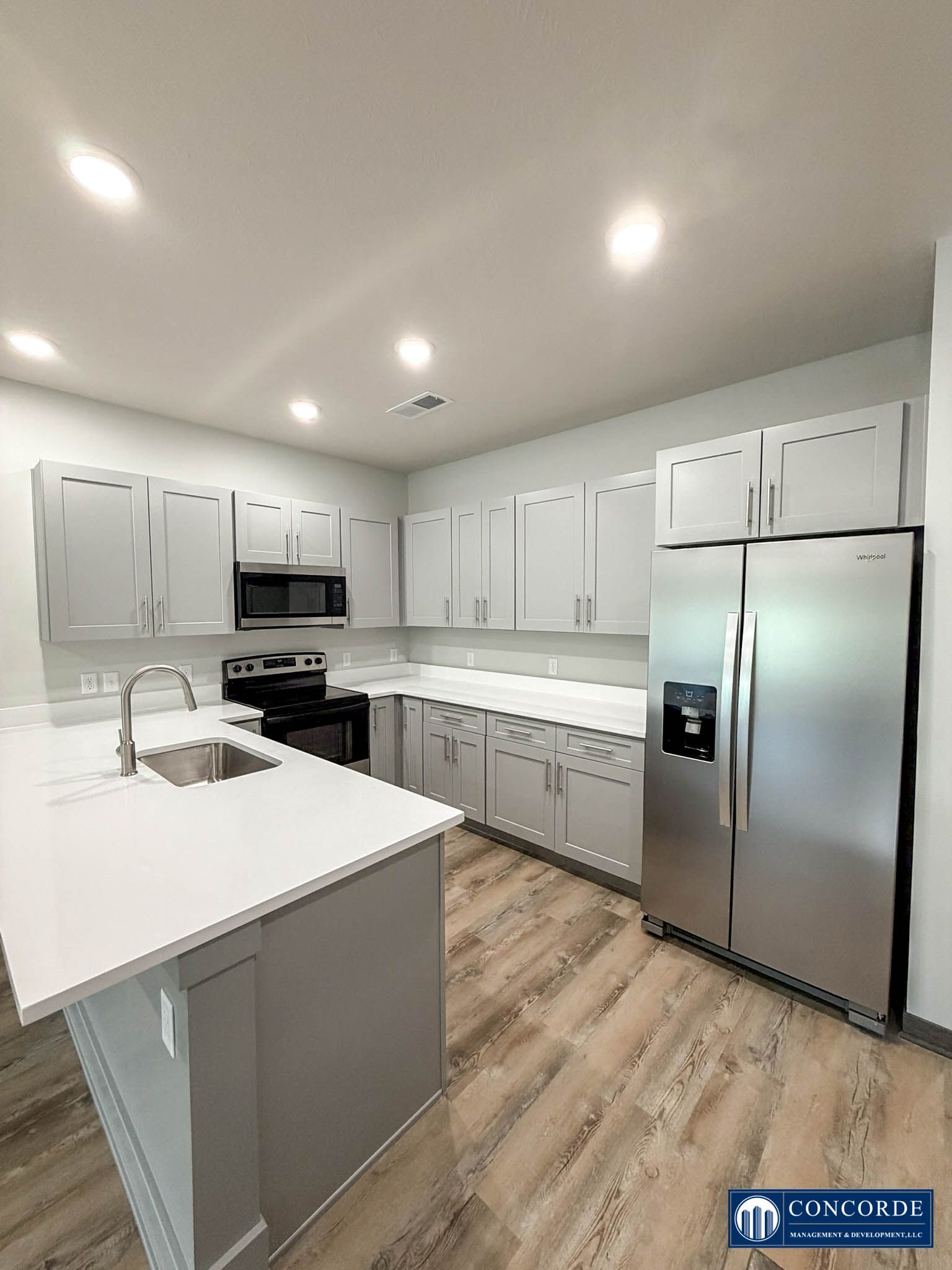 Bright white modern kitchen with stainless steel appliances, island, and wood-look flooring
