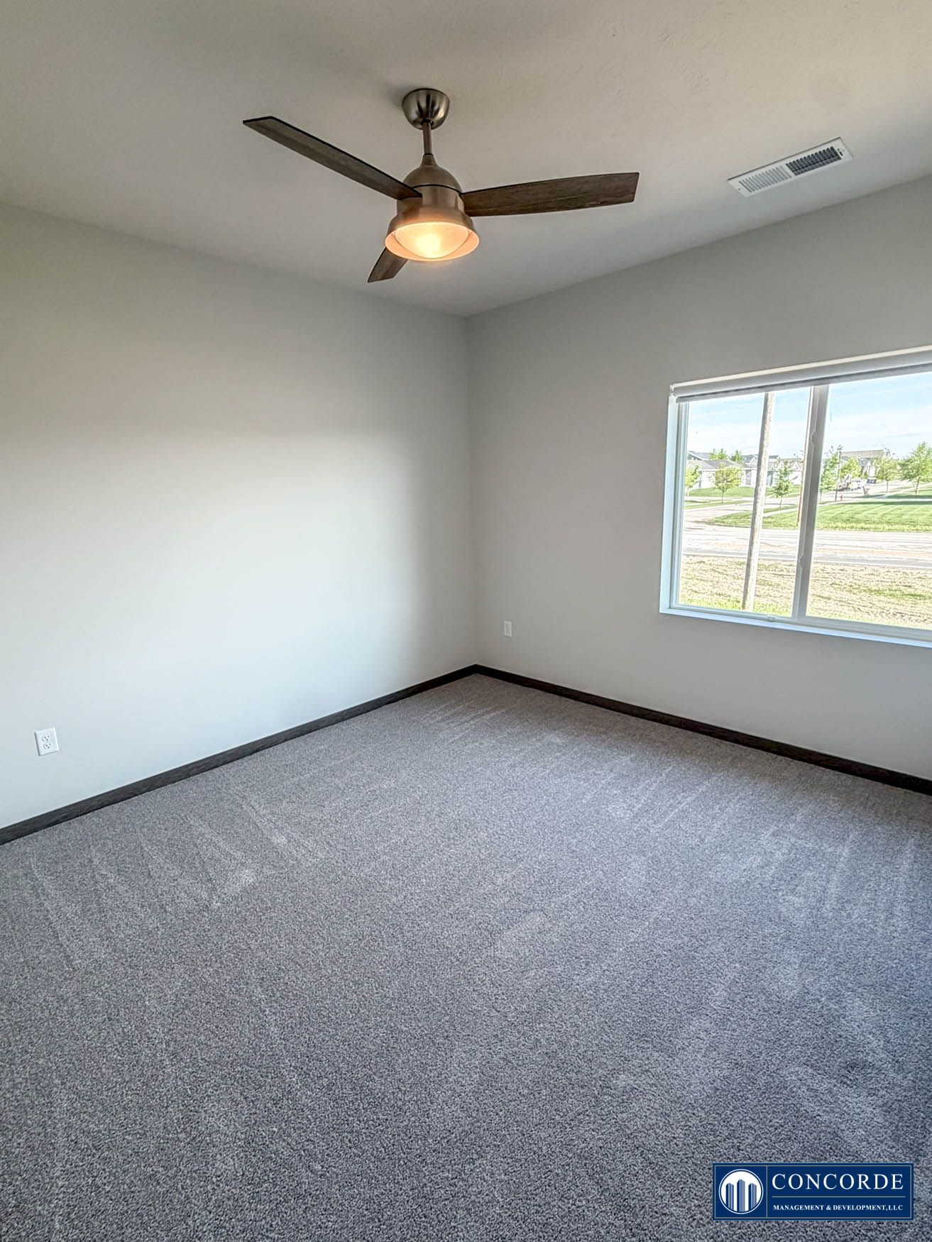 Empty bedroom with gray carpet, white walls, ceiling fan, and a window letting in natural light