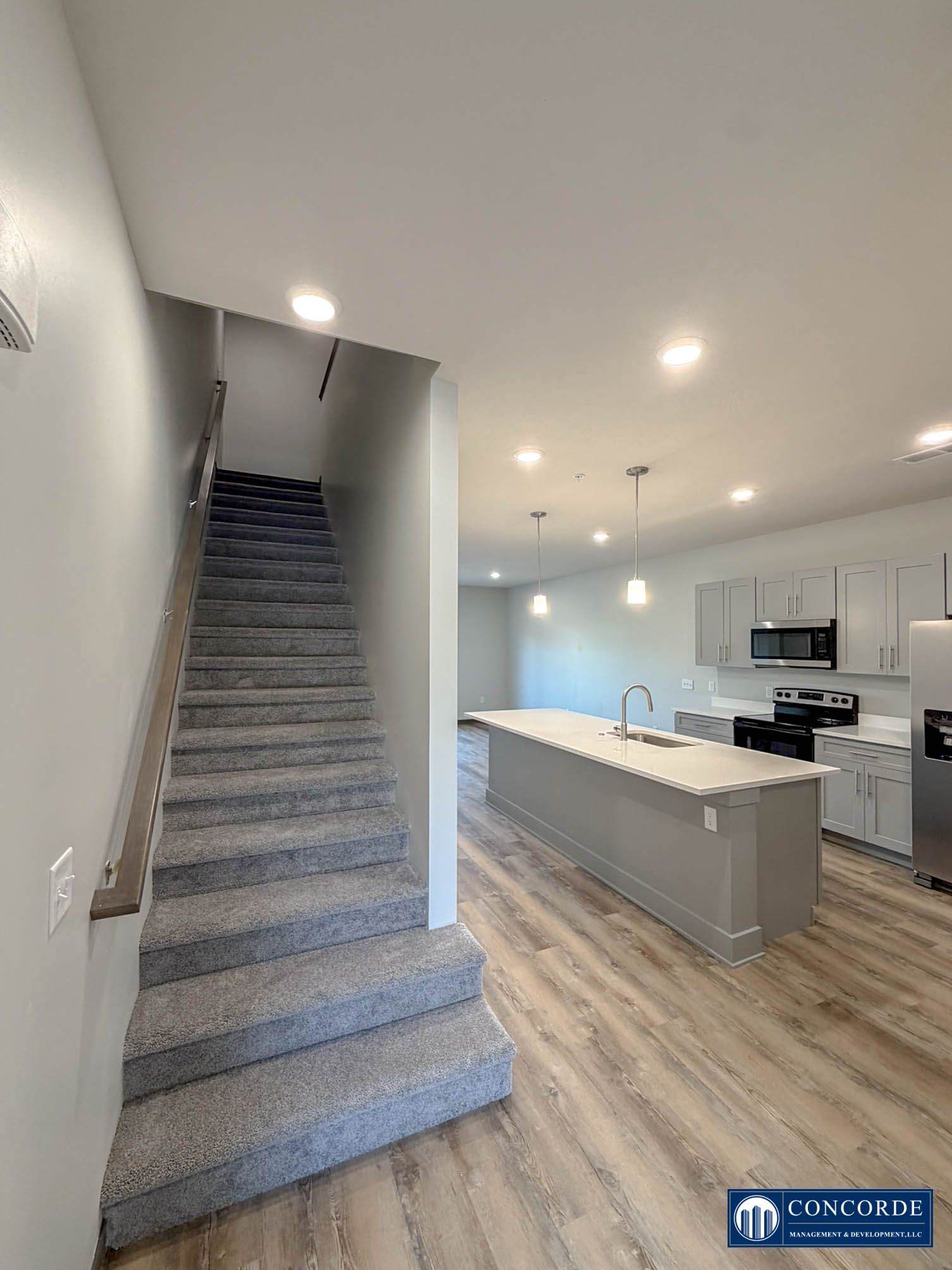 Open-concept kitchen with island and pendant lights beside carpeted stairs in a modern home