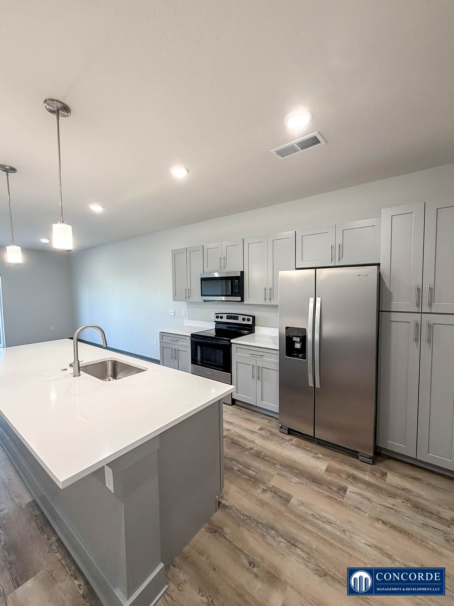 Bright modern kitchen with white island, stainless steel appliances, and wood-look flooring