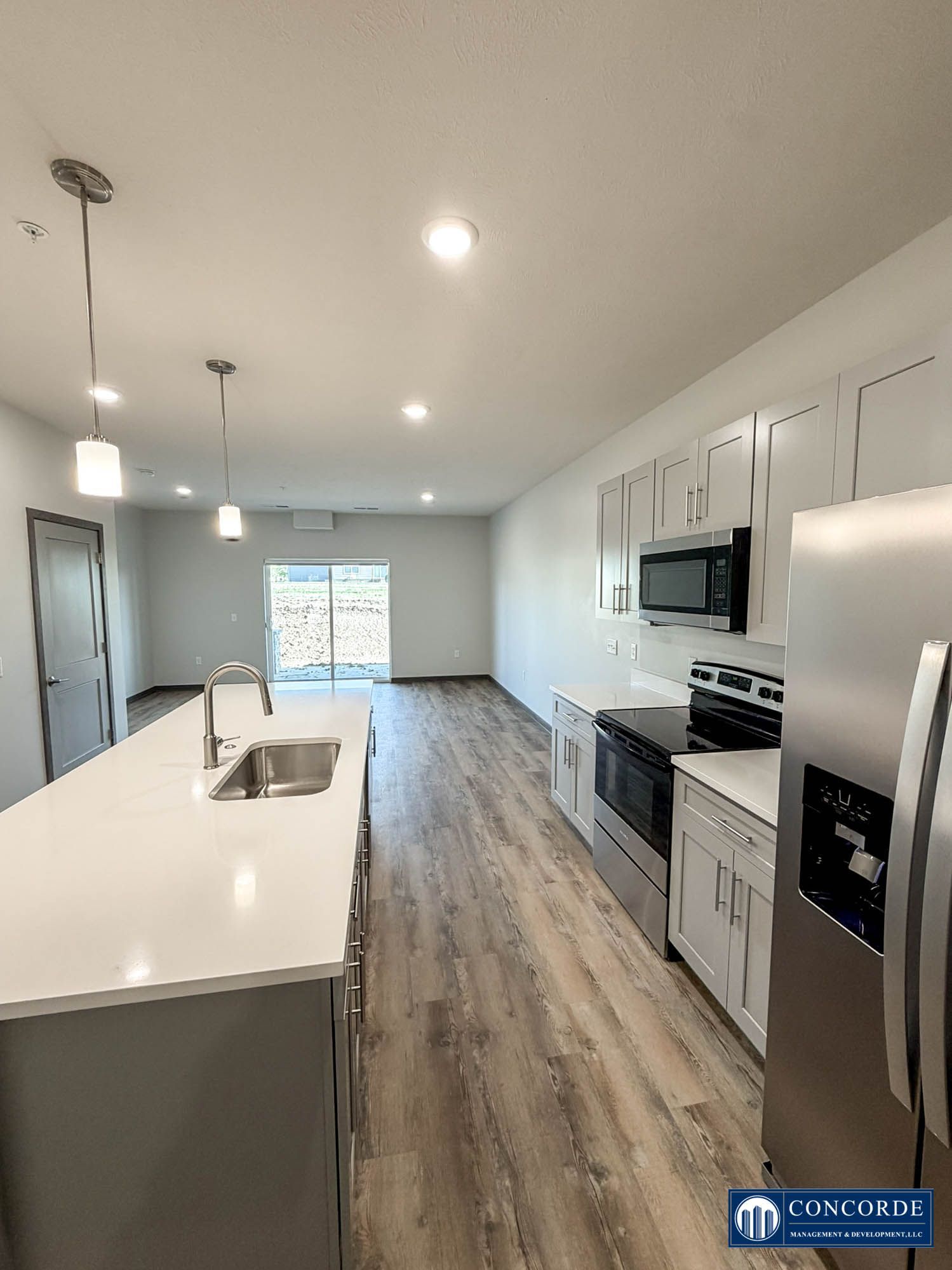 Modern white kitchen with island, stainless steel appliances, and sliding glass door to the backyard.