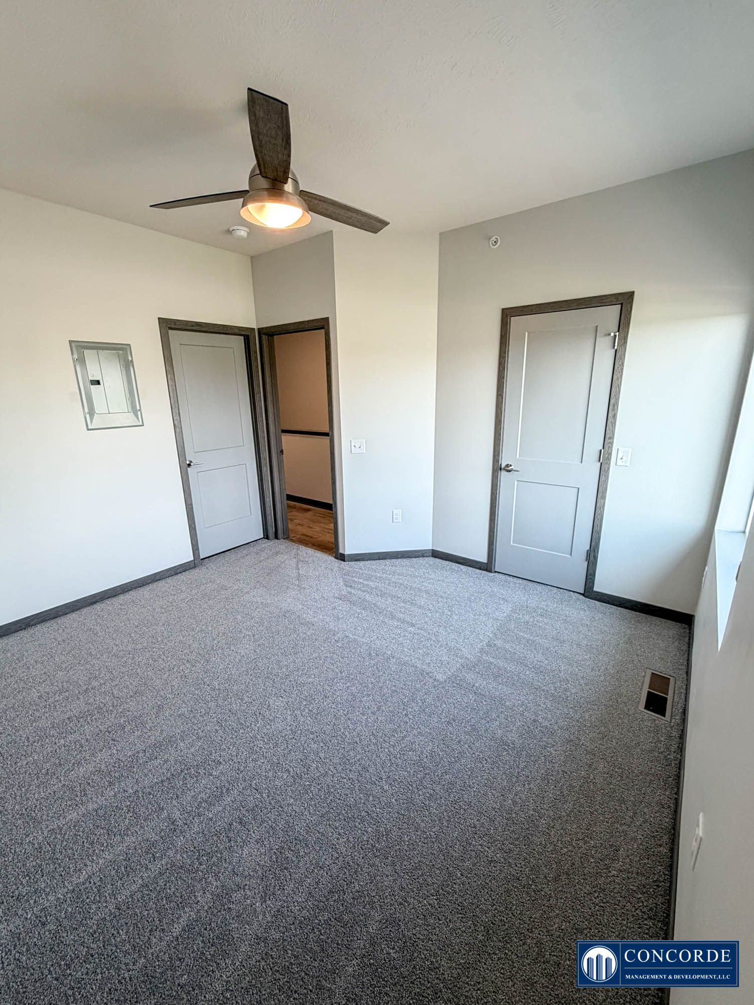 Empty carpeted bedroom with ceiling fan, closet doors, and white walls
