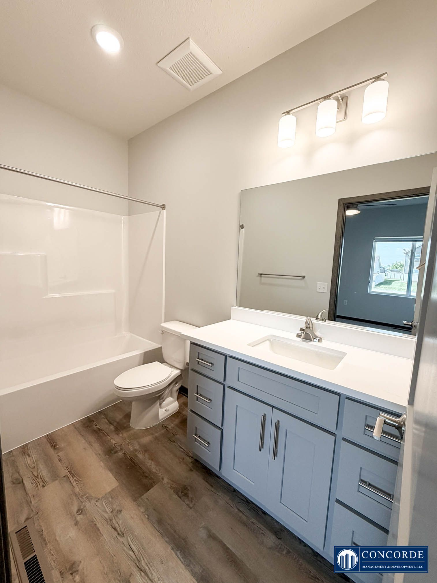 Modern bathroom with blue vanity, white tub, toilet, and window over the sink