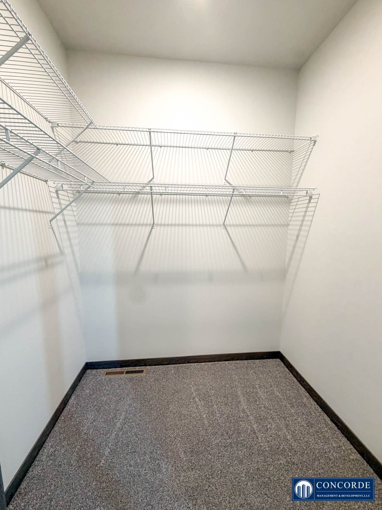 Empty walk-in closet with white wire shelves and gray carpet floor