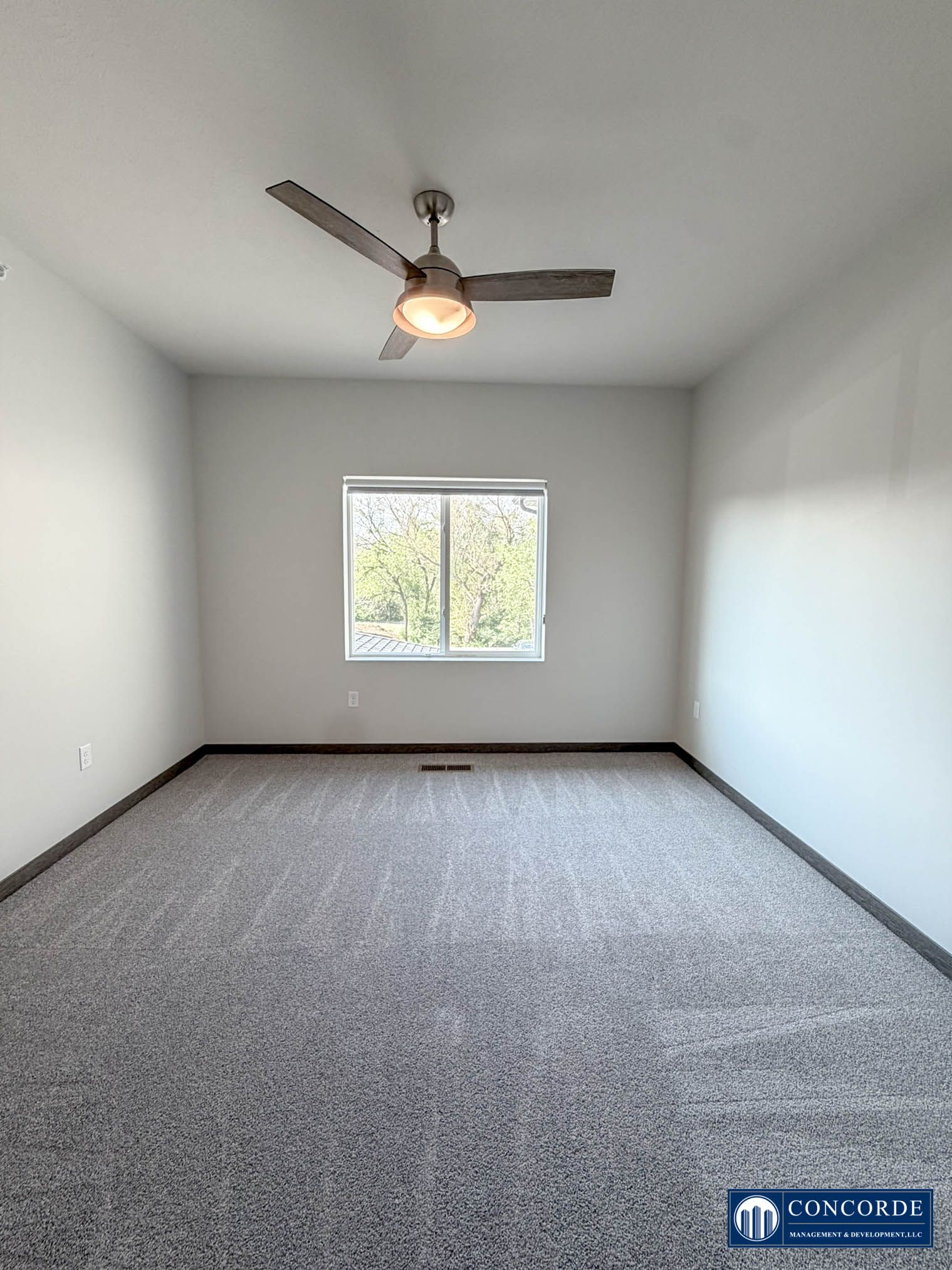 Empty carpeted bedroom with a ceiling fan and a window.