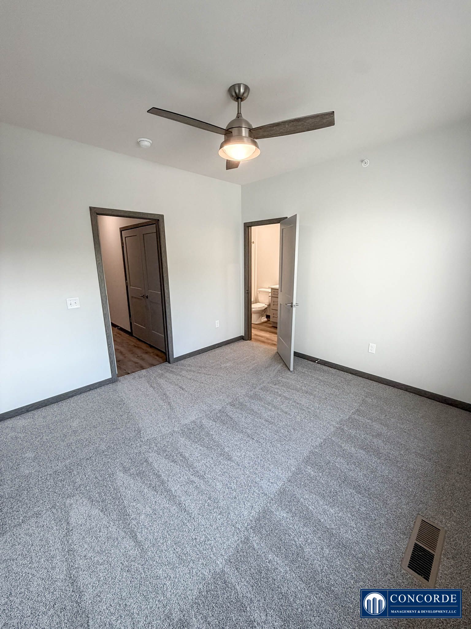 Empty carpeted bedroom with ceiling fan, two doorways, and light gray walls