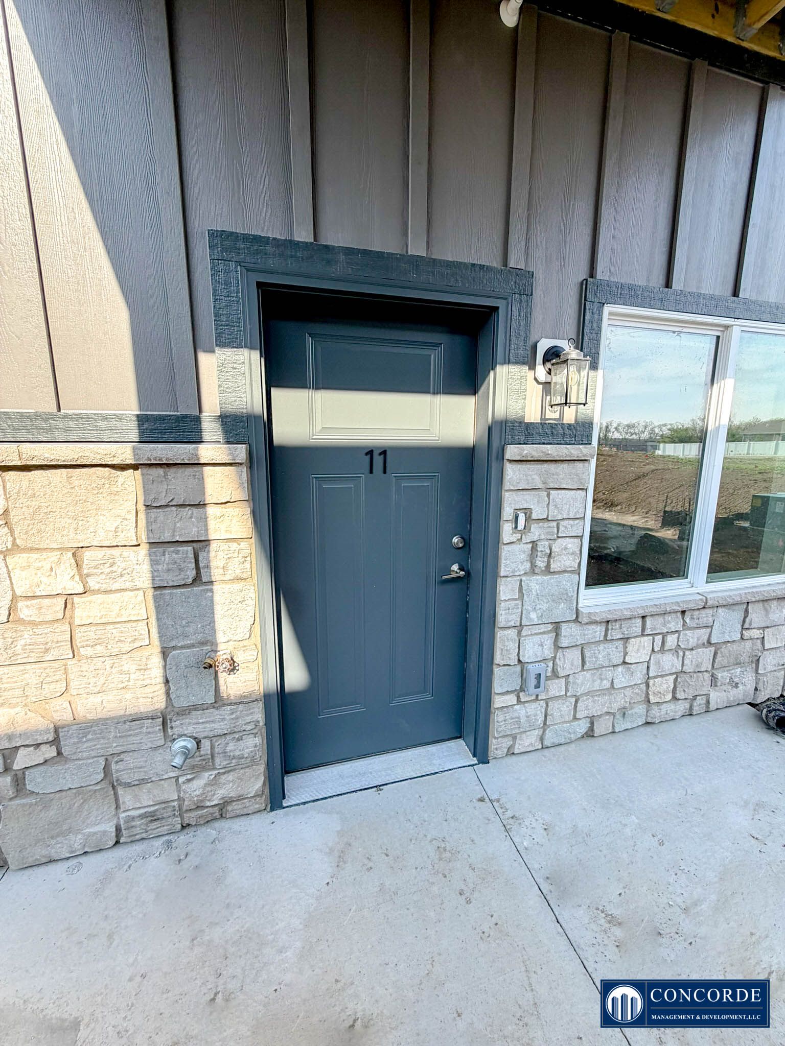 Dark gray front door set in a stone-and-wood exterior wall beside a window.