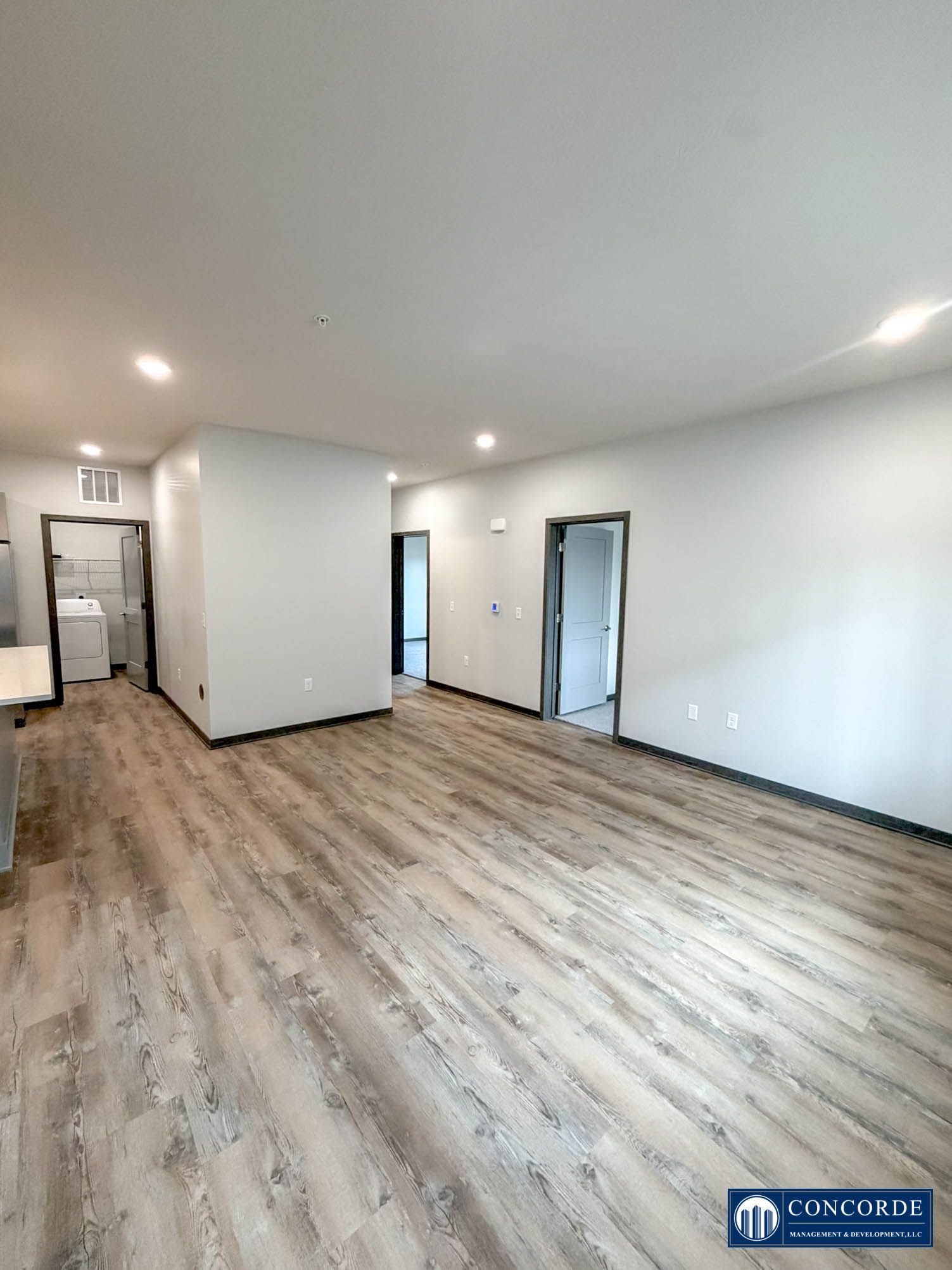 Empty modern room with light wood floors, white walls, recessed lights, and multiple doorways