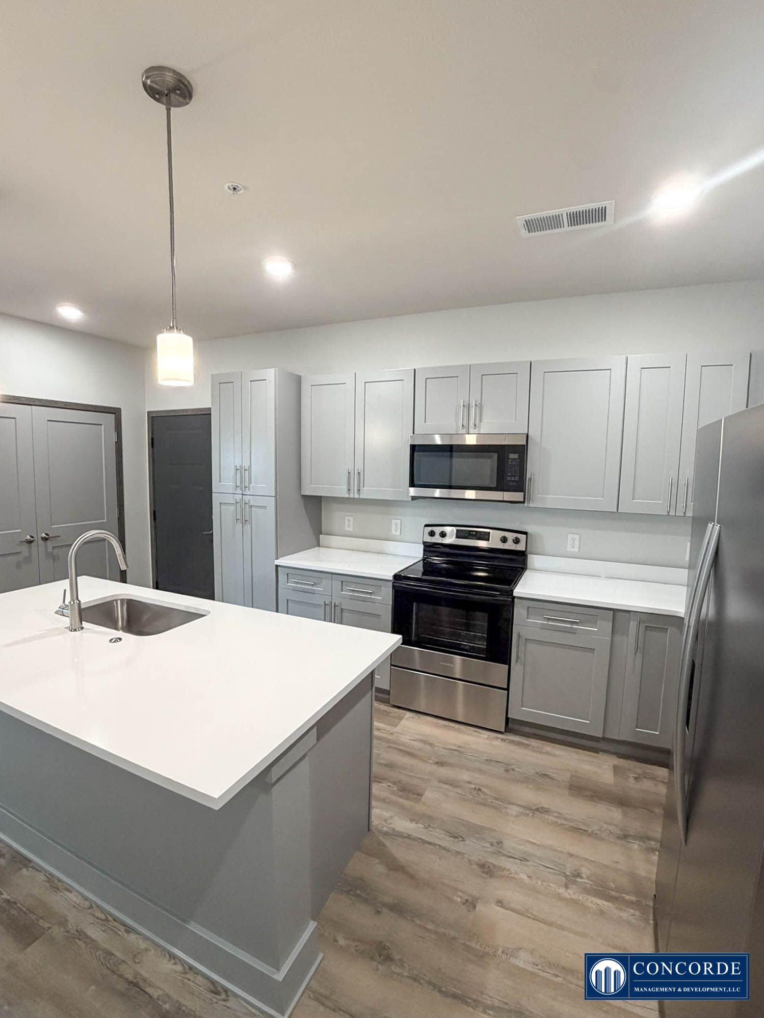 Modern kitchen with white cabinets, gray island, stainless appliances, and wood-look flooring