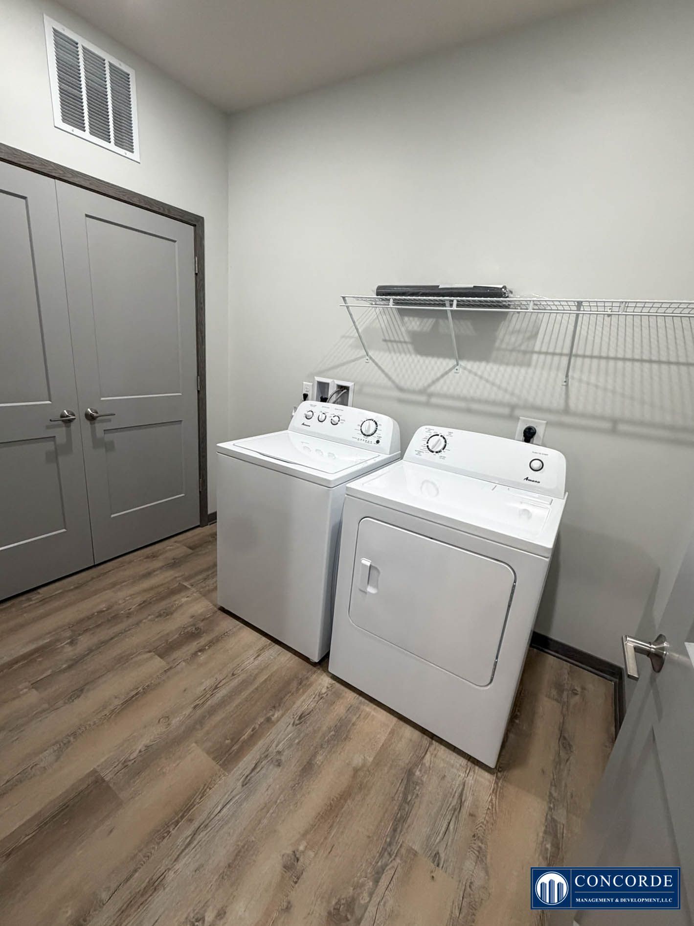 Laundry room with washer and dryer, gray double doors, and wire shelving on the wall.
