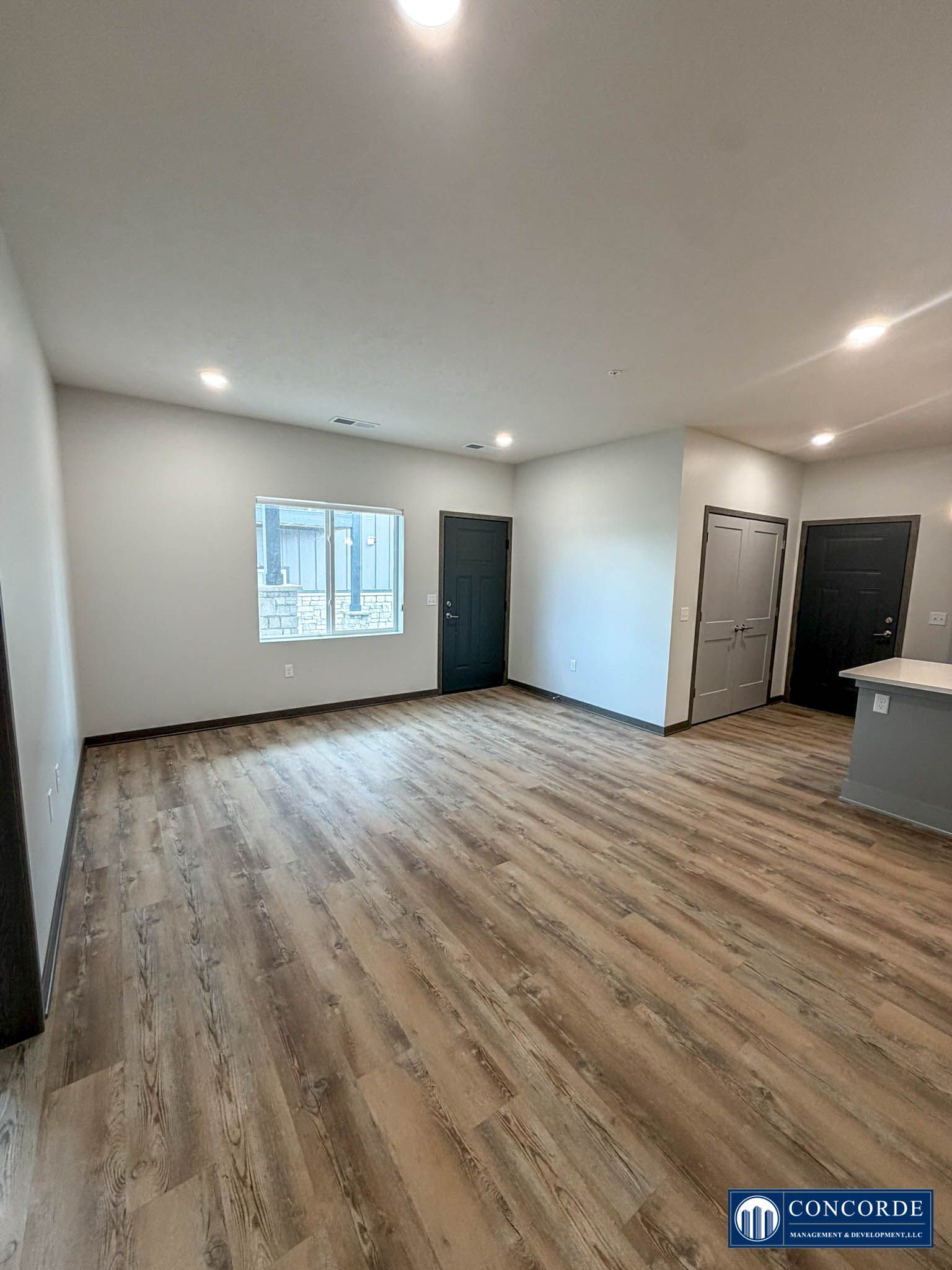 Empty unfurnished room with wood-look floor, white walls, window, and dark doors