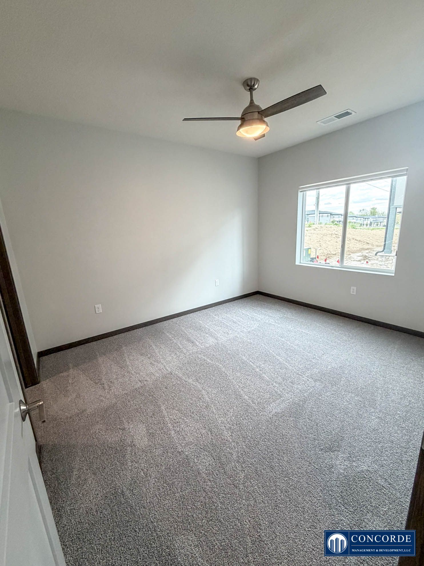 Empty gray bedroom with carpet, ceiling fan, and a window letting in daylight.