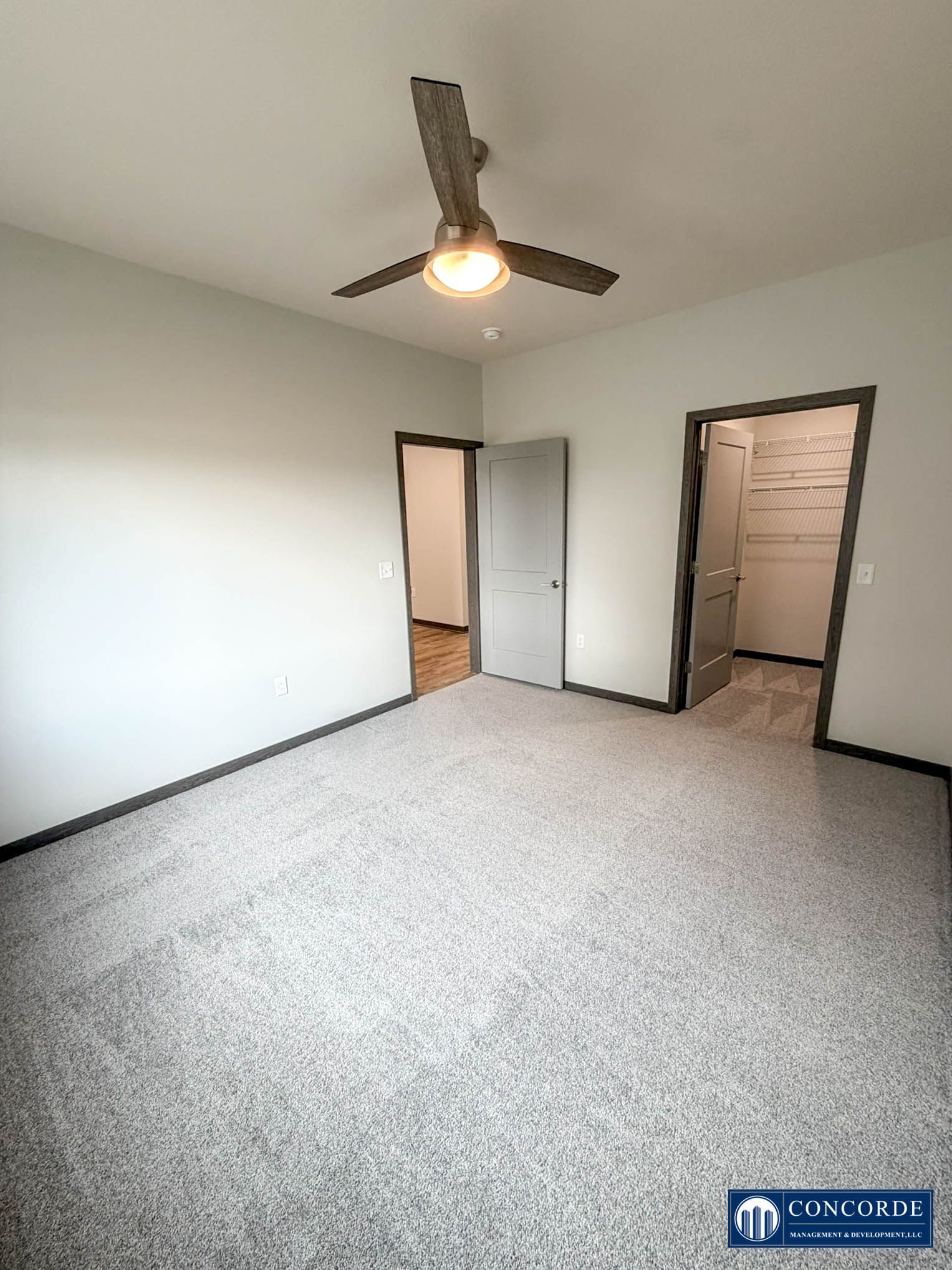Empty carpeted bedroom with white walls, ceiling fan, and two open doorways.