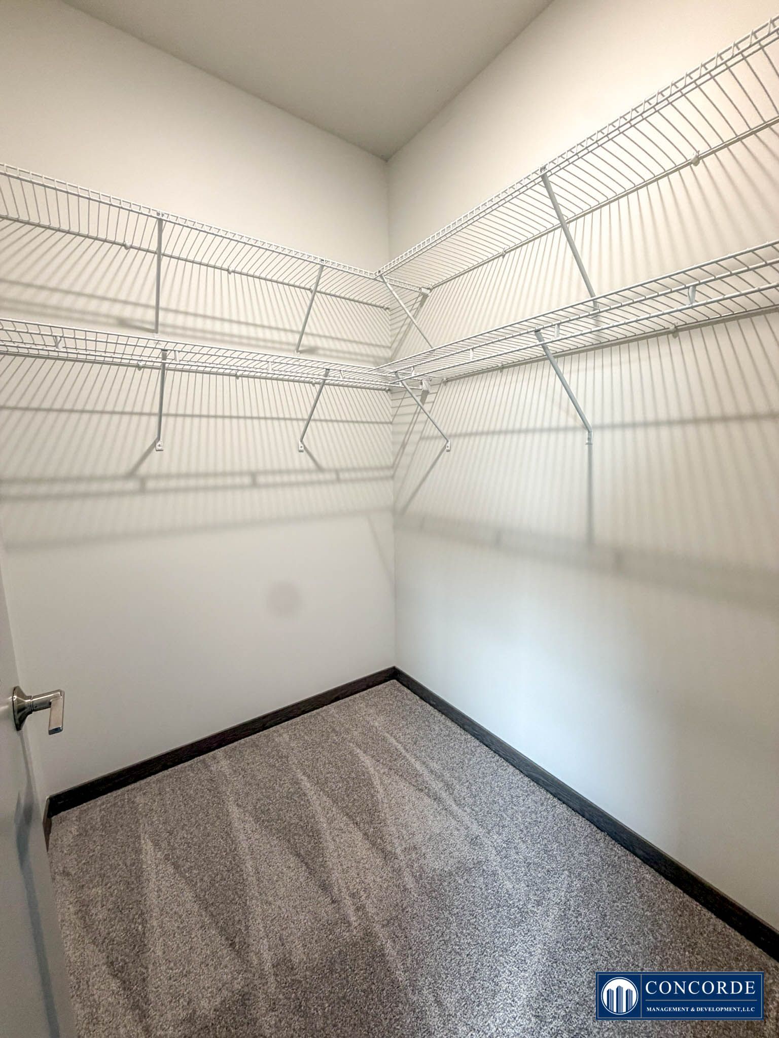 Empty walk-in closet with white wire shelving and speckled carpet flooring