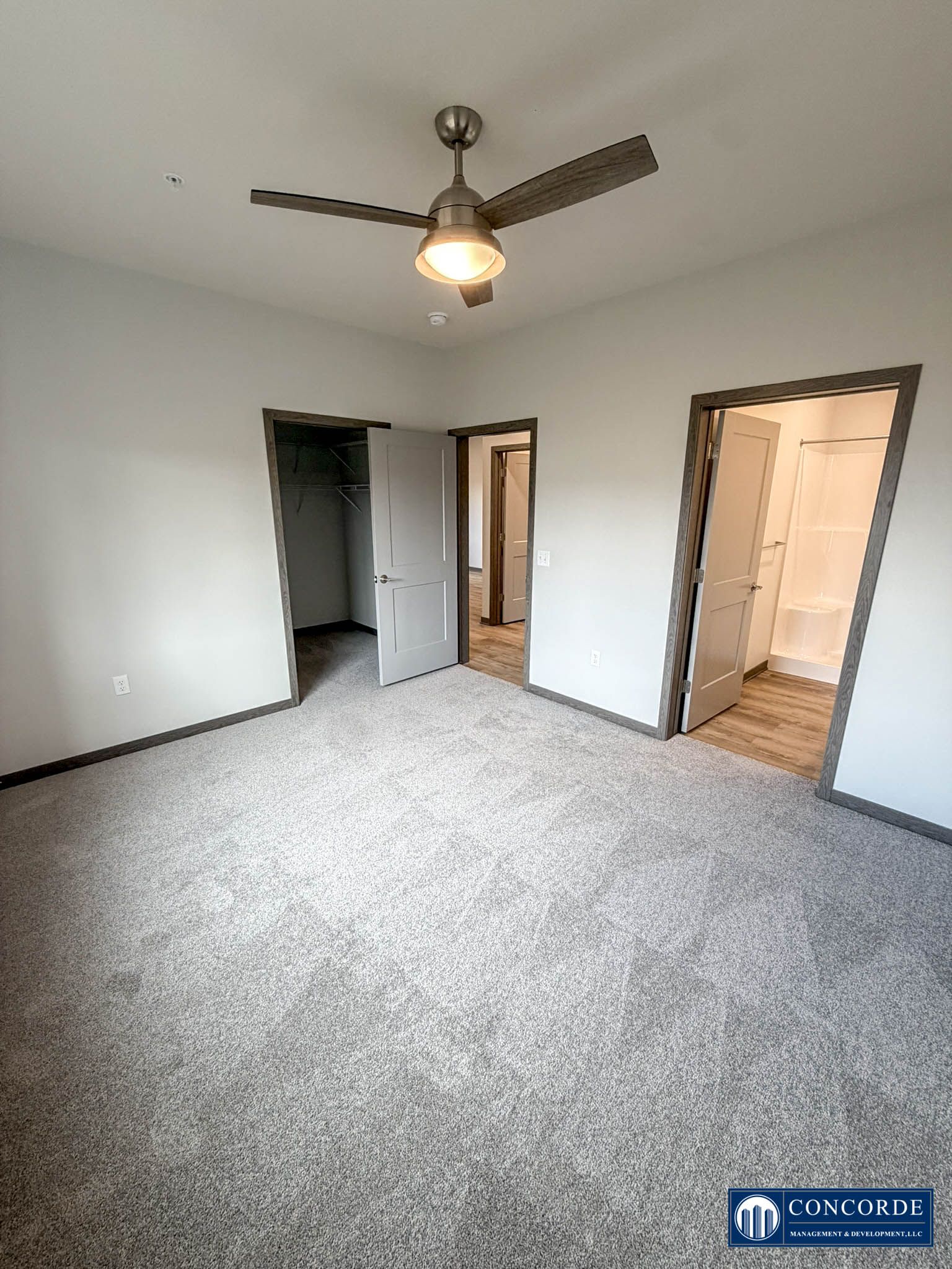 Empty carpeted bedroom with ceiling fan, white walls, and doorway to a bathroom or closet.
