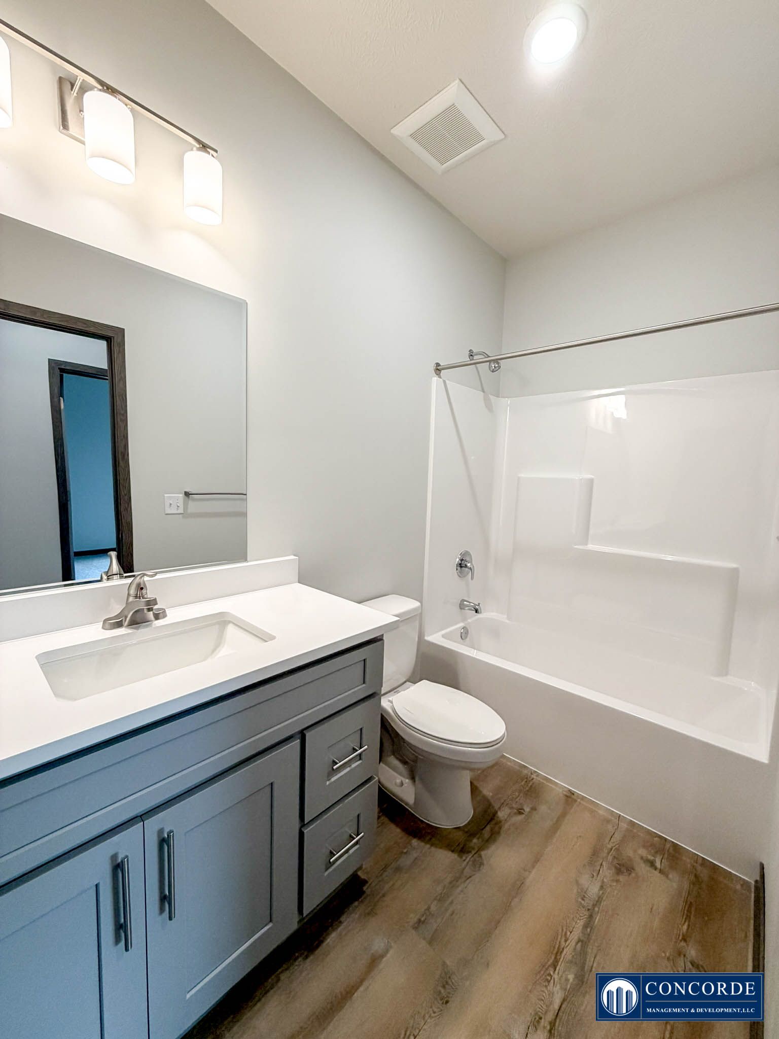 Bright white bathroom with blue vanity, mirror, toilet, and tub shower combo