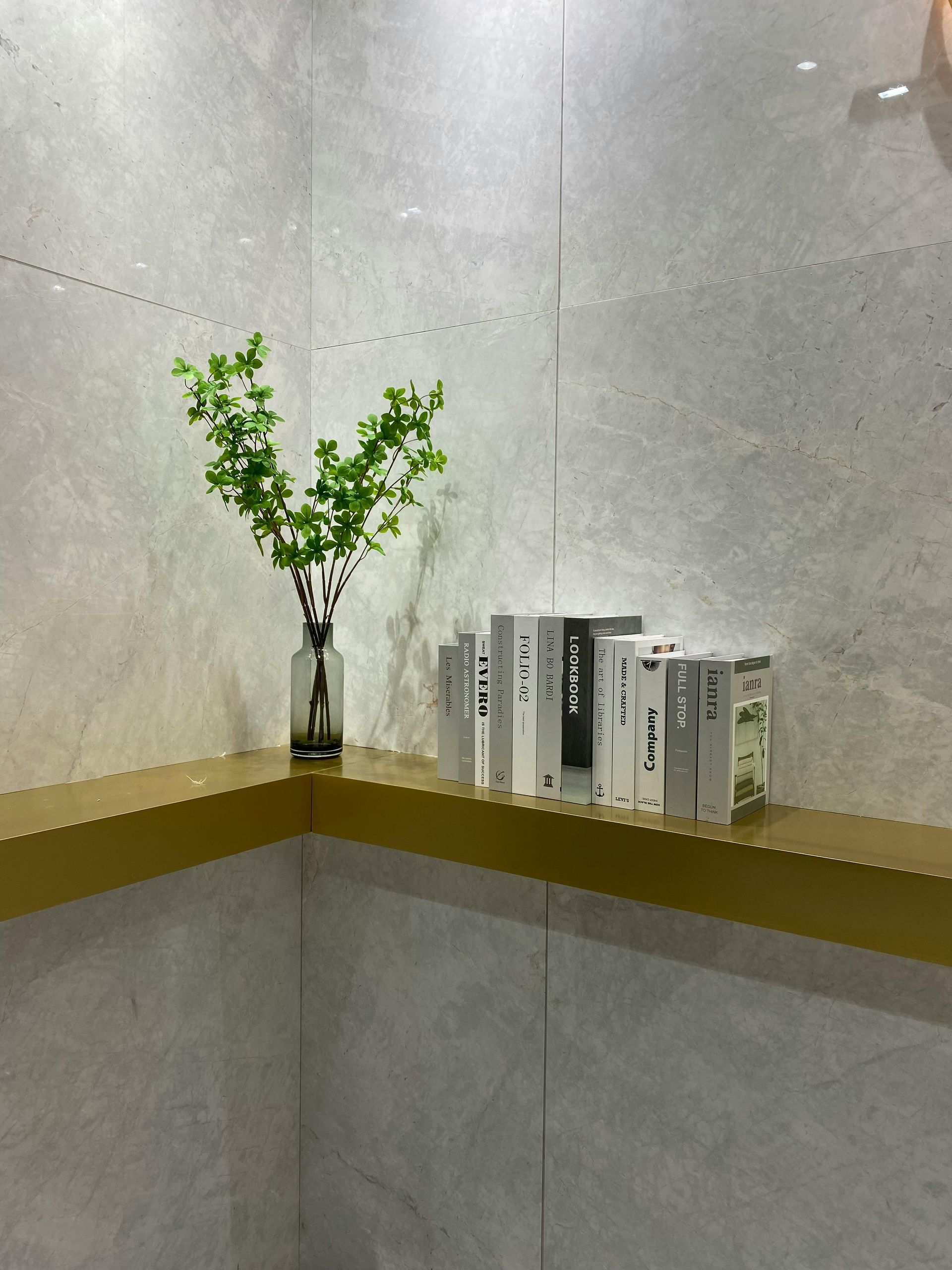 Vase with green branches and white books on a corner shelf against a gray wall