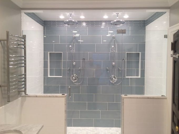 A bathroom with a walk in shower with blue tiles and a glass door.