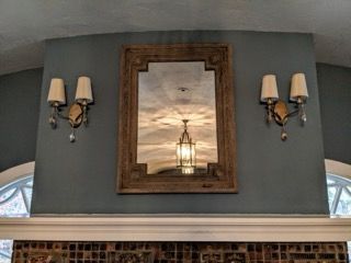A mirror is hanging on a wall above a fireplace.