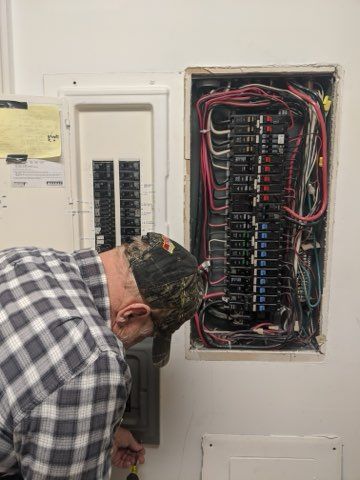 A man in a plaid shirt is working on an electrical box.