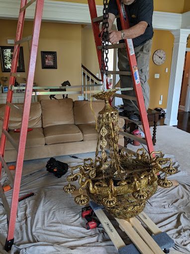 A man is standing on a ladder fixing a chandelier in a living room.