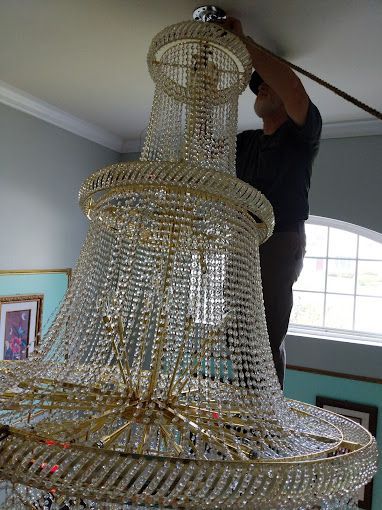 A man is hanging a chandelier from the ceiling in a room.