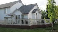 A two-story white house with a brown deck in a grassy yard.