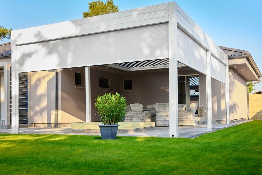 White pergola shading a patio with gray awnings and a potted plant on a green lawn.