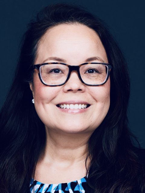 Woman wearing glasses, smiling, with dark hair, looking at the camera.