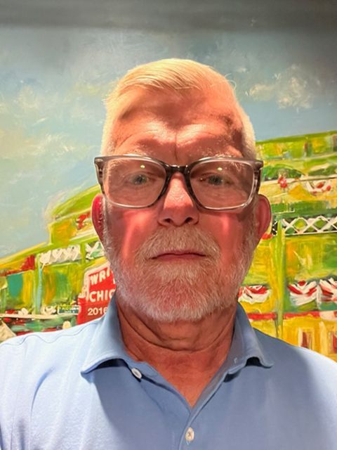 Man with glasses and white hair against a colorful backdrop, wearing a light blue polo shirt.