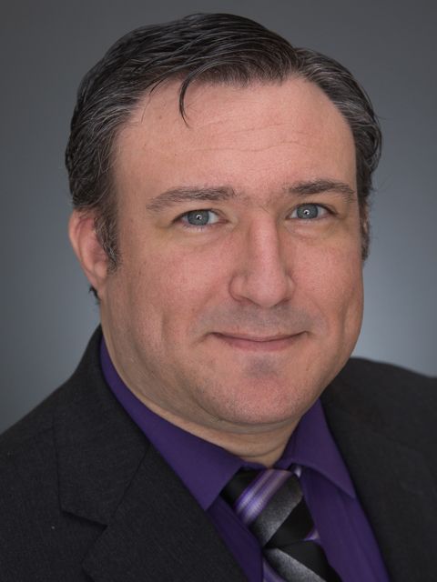Man in suit and purple shirt smiles at camera.