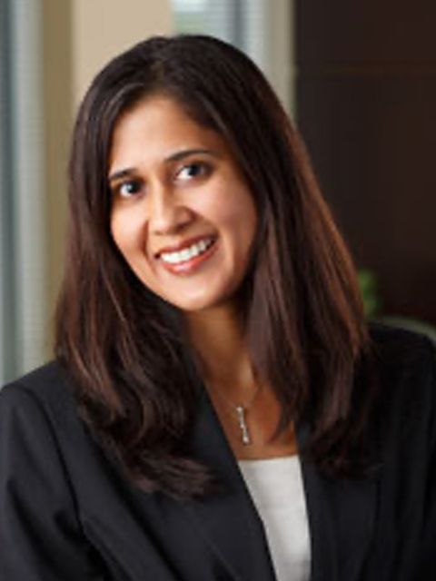 Woman with long dark hair smiles, wearing a black blazer and white top.